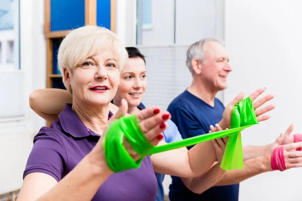 Physio zeigt Senioren-Paar, wie man Gummiband als Expander verwendet — Stockfoto