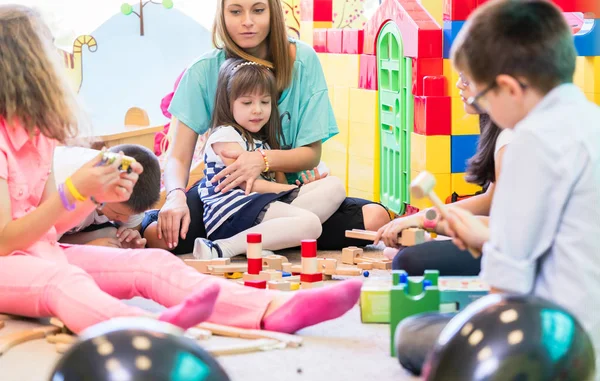 Dedicado jardim de infância professor segurando uma menina tímida enquanto assiste — Fotografia de Stock