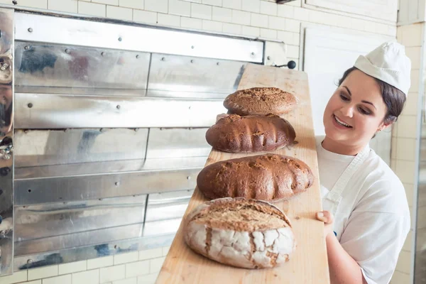 Bäckerin präsentiert in Backstube Brot an Bord — Stockfoto