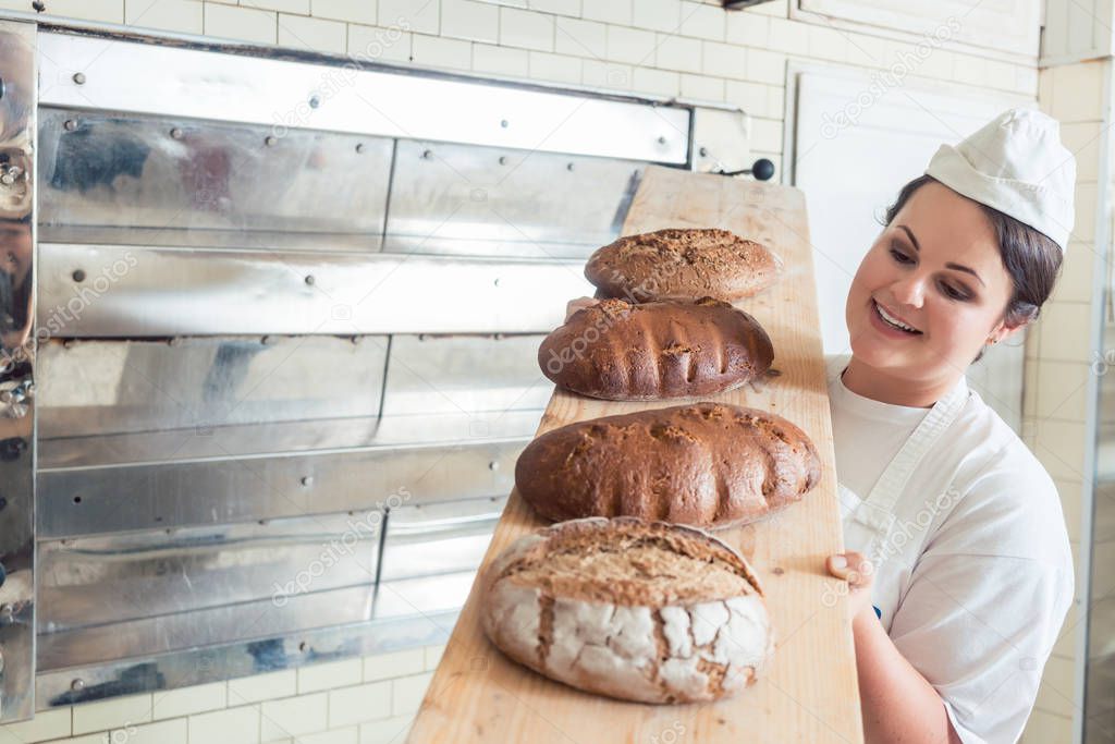 Baker woman presenting bread on board in bakery — Stock Photo © Kzenon