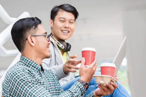 Dois jovens homens asiáticos usando um laptop enquanto relaxam durante o intervalo — Fotografia de Stock