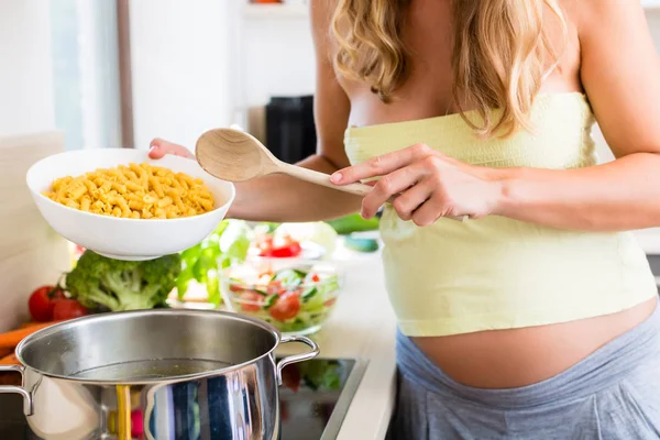 Беременная женщина готовит макароны на кухне — стоковое фото