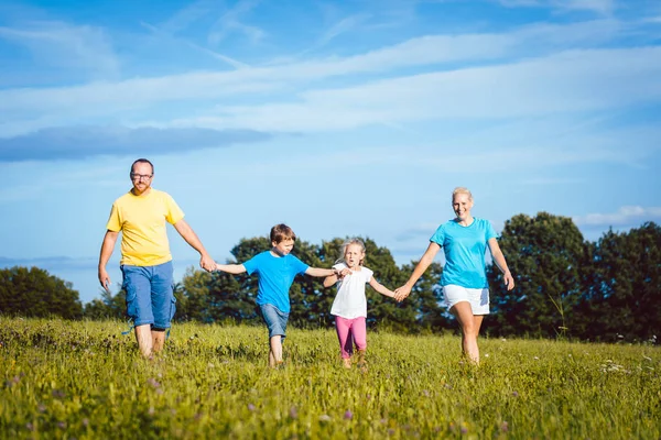 Family holding hands running over meadow — Stock Photo, Image