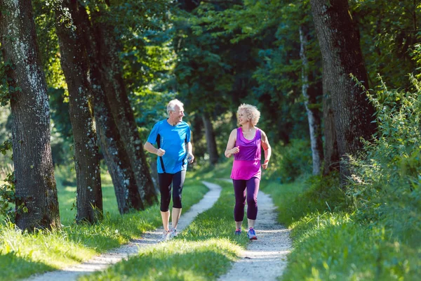 Two active seniors with a healthy lifestyle smiling while joggin — Stock Photo, Image