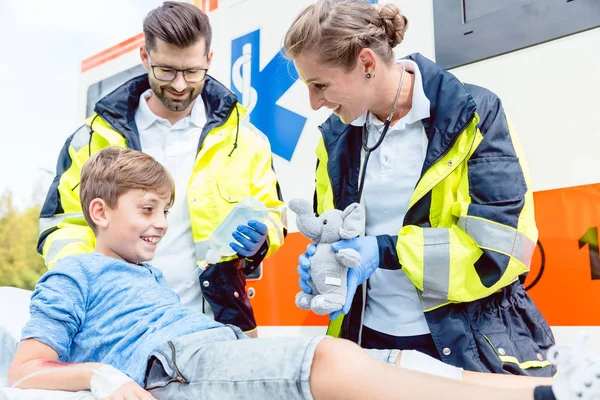 Emergency medic giving soft toy to console injured boy — Stock Photo, Image