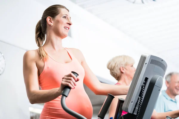 Mujer embarazada entrenando en cross trainer en el gimnasio — Foto de Stock