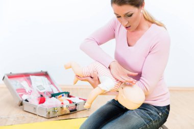 Woman in first aid course practicing revival of infant on baby d clipart