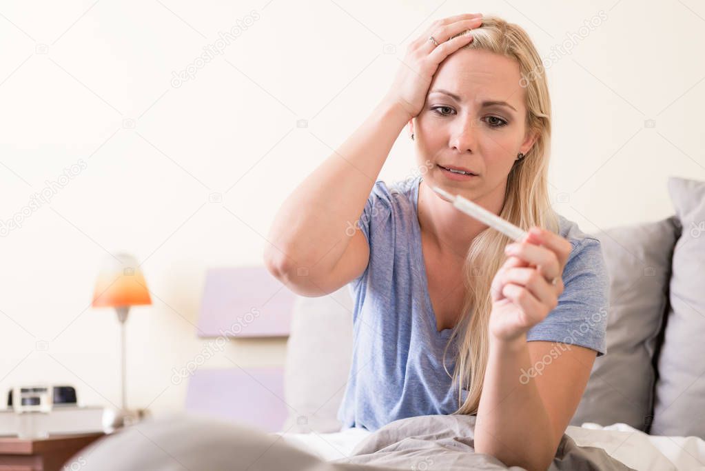 Sick woman with fever checking her temperature