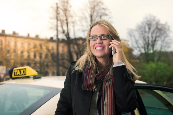 Young woman in front of taxi with phone — Stock Photo, Image