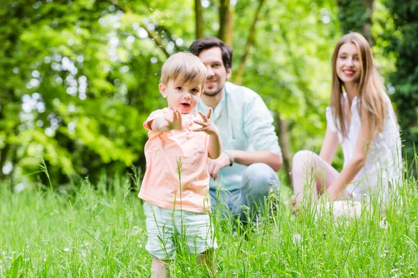 Little boy running over meadow with family in back — Stock Photo, Image