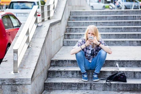 Молодая белая женщина, сидя на лестнице, пользуется смартфоном — стоковое фото