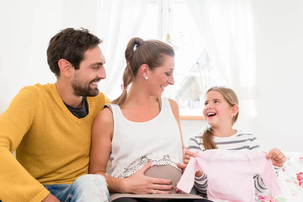 Perhe odottaa jälkeläisiä ja katselee vauvan vaatteita — kuvapankkivalokuva