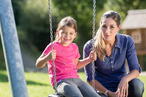 Vrouw met lachen meisje op schommel plezier samen — Stockfoto