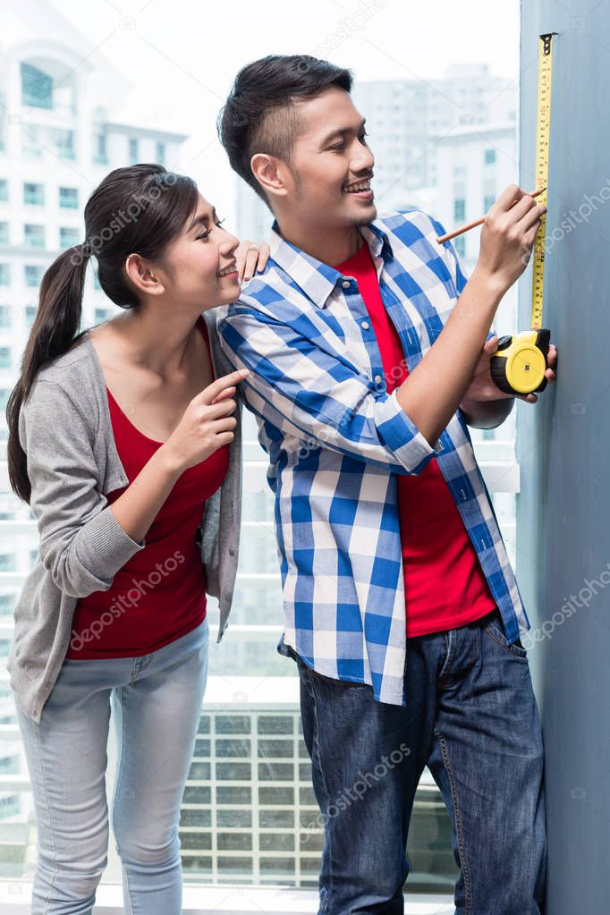 Young indonesian couple measuring walls in new apartment