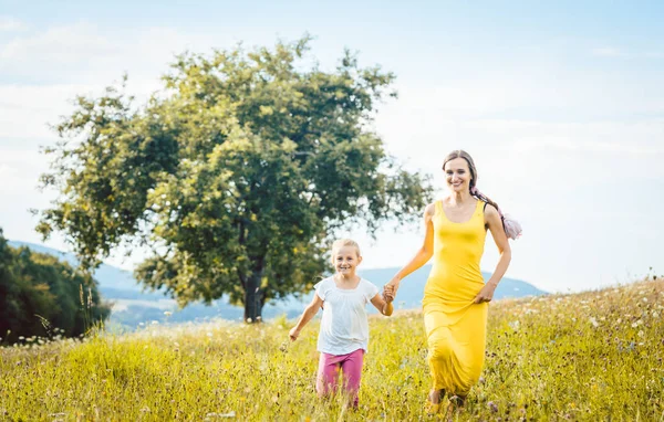 Mãe com sua filha correndo em um prado de verão — Fotografia de Stock