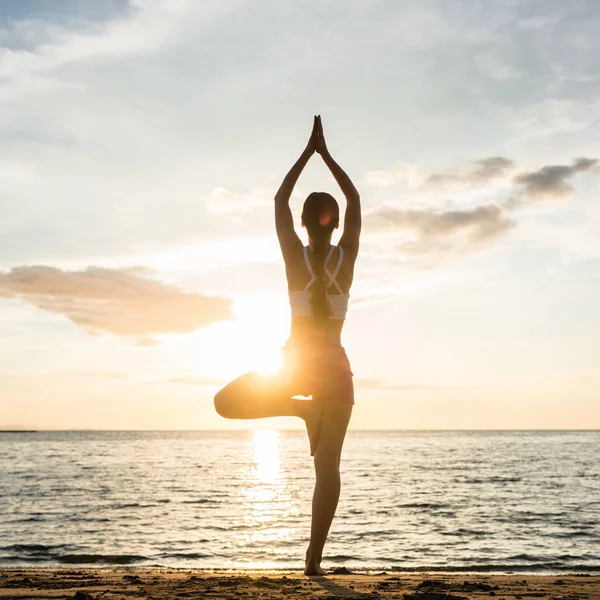 Silhouette di una donna che pratica la posa albero yoga su una spiaggia a — Foto Stock