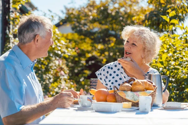 Senior woman and man having breakfast sitting in their garden ou — Stock Photo, Image