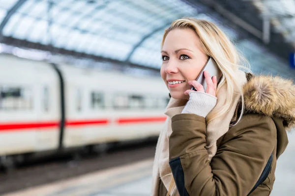 Woman using her telephone while train arrives in station