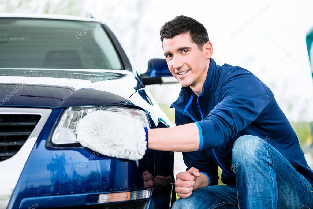 Smiling man cleaning the headlamp on his car