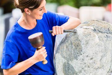 Stonemason working on boulder with sledgehammer and iron clipart