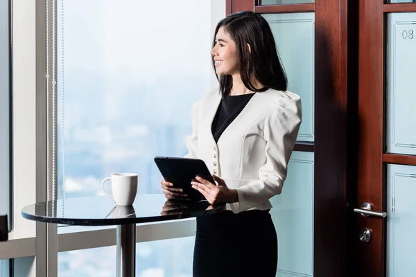 Geschäftsfrau steht am Fenster eines Wolkenkratzers mit Blick auf die Skyline — Stockfoto