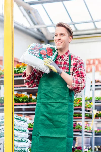 Fröhlicher junger Mann mit einem Sack Blumenerde bei der Arbeit — Stockfoto