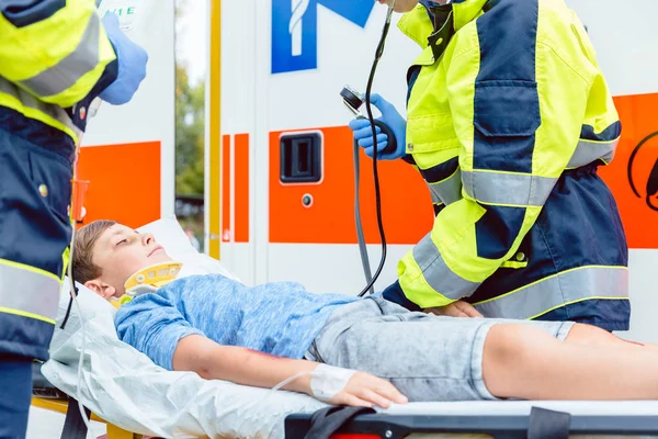 Médecins d'urgence mettant garçon blessé en ambulance — Photo