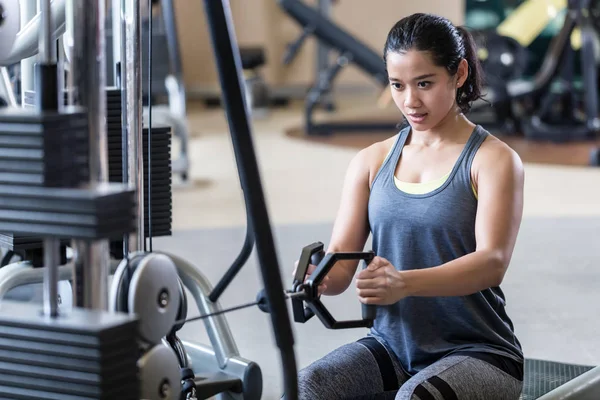 Strong and beautiful woman rowing at the cable machine during workout — Stock Photo, Image