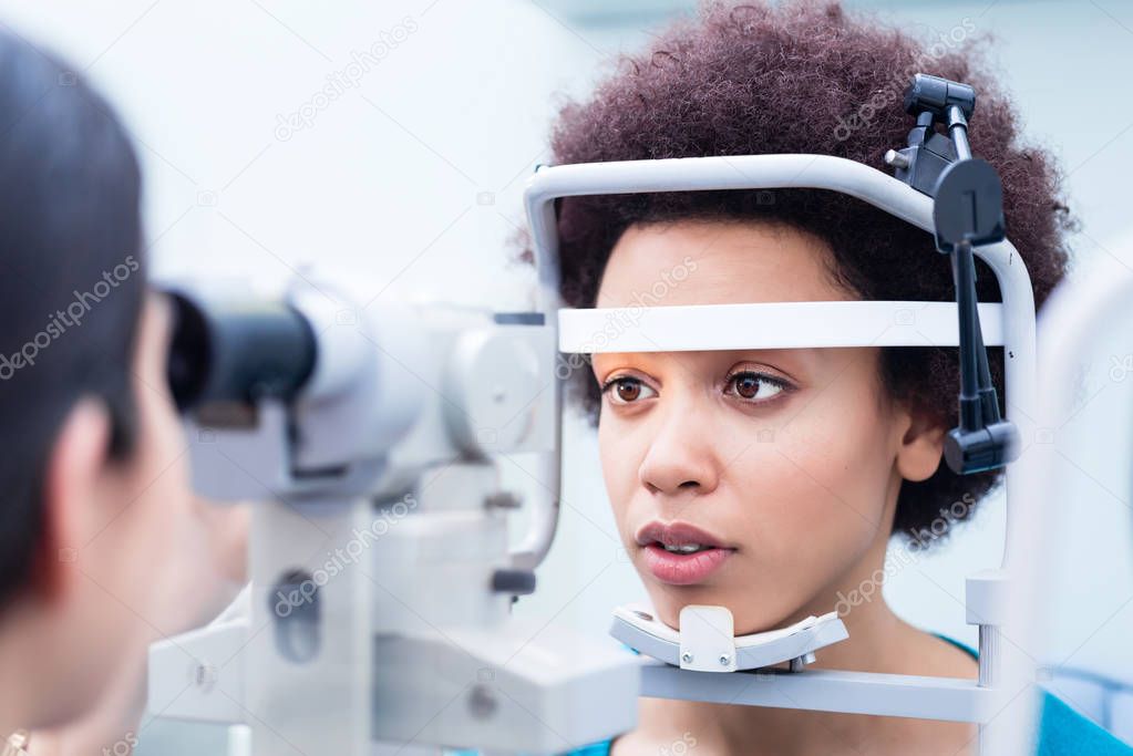Optician measuring woman eyes with refractometer in optician shop