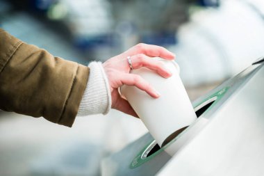 Atık ayrıştırma kabı kullanan kadın köpükten yapılmış kahve bardağını atıyor. 