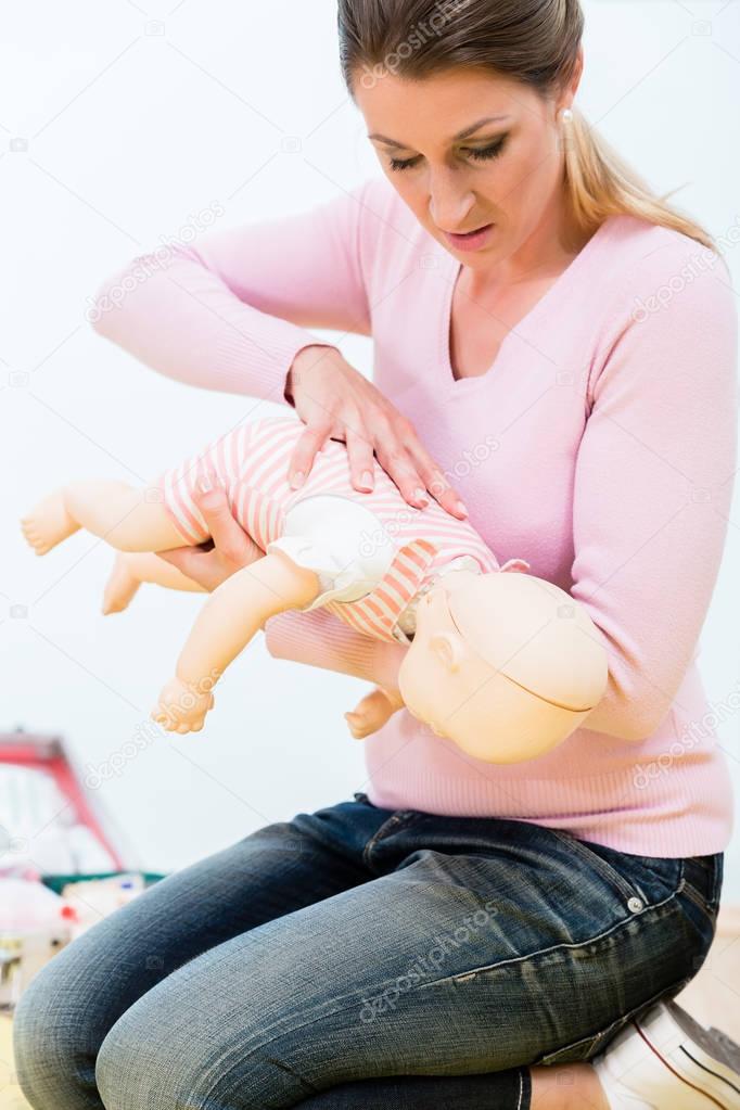 Woman practicing revival of infant on baby doll in first aid course 