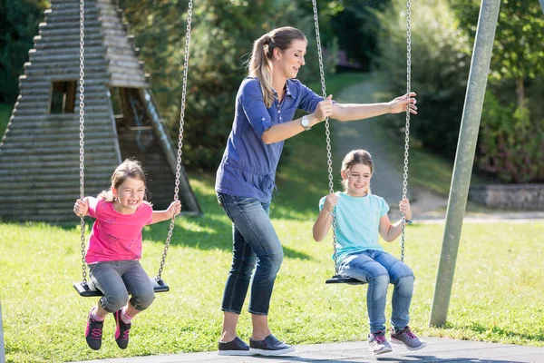 Familia con dos niñas y madre en el columpio del patio — Foto de Stock