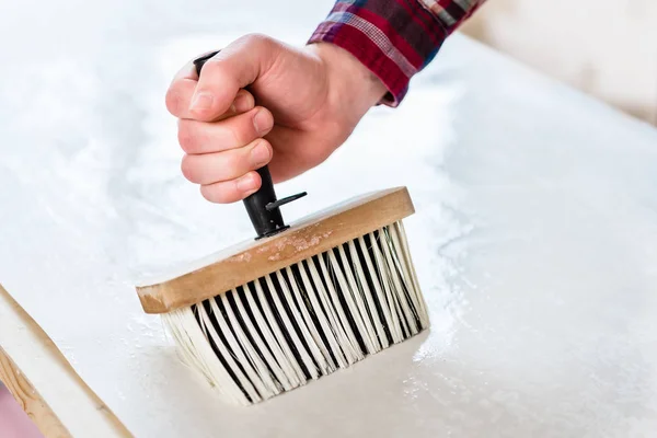 Hand eines Mannes, der einen synthetischen Pinsel hält, während er Kleister aufträgt — Stockfoto