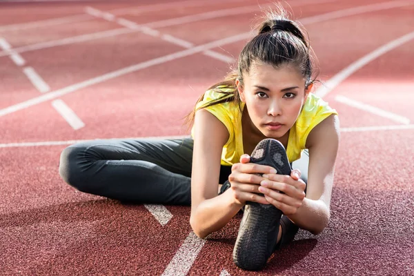 Vrouw atleet, die zich uitstrekt over racing track voordat u — Stockfoto