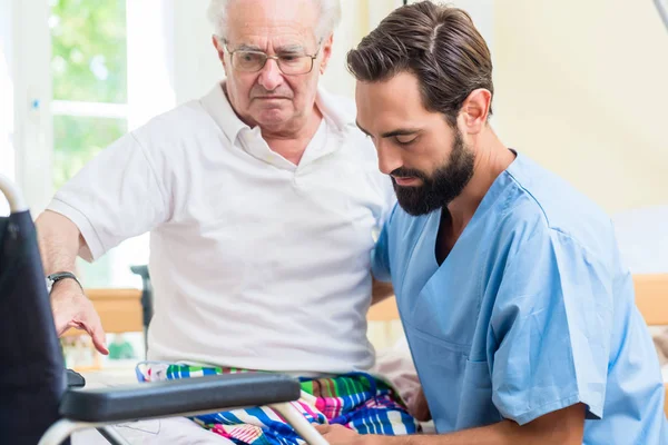 Äldreomsorg sjuksköterska hjälper senior från säng till rullstol — Stockfoto