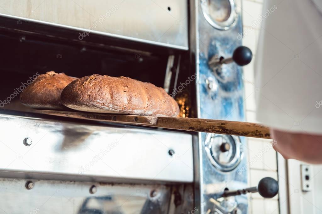 Baker getting fresh bread with shovel out of oven
