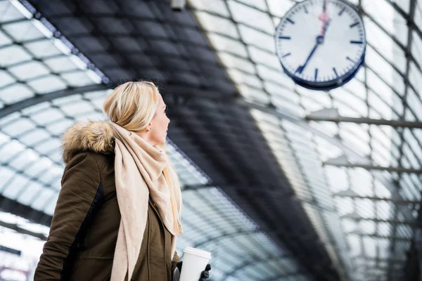 Woman looking at clock in train station as her train has a delay — Stock Photo, Image