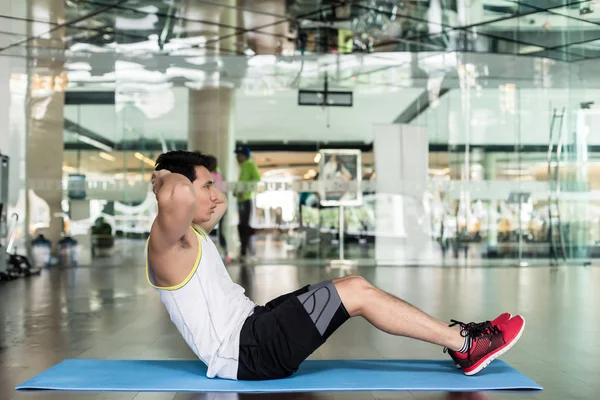 Hombre joven sentado mientras hace abdominales para los músculos abdominales — Foto de Stock