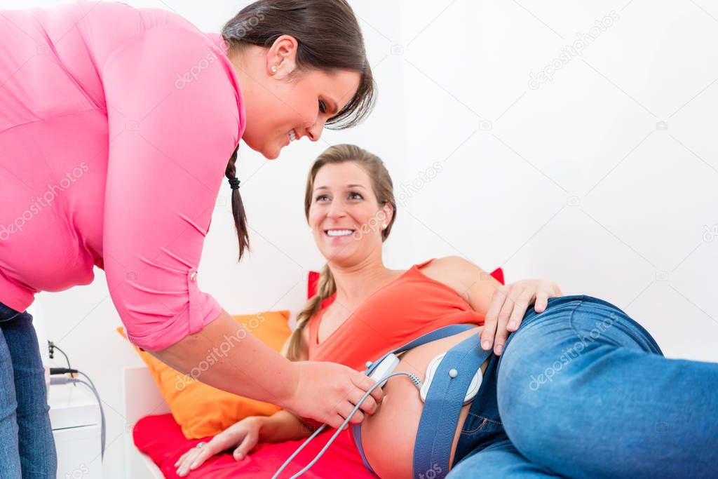 Smiling expectant mother and midwife adjusting cardiotocograph