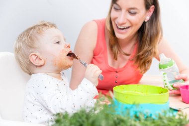 Portrait of a cute baby sitting on high chair while eating solid food clipart