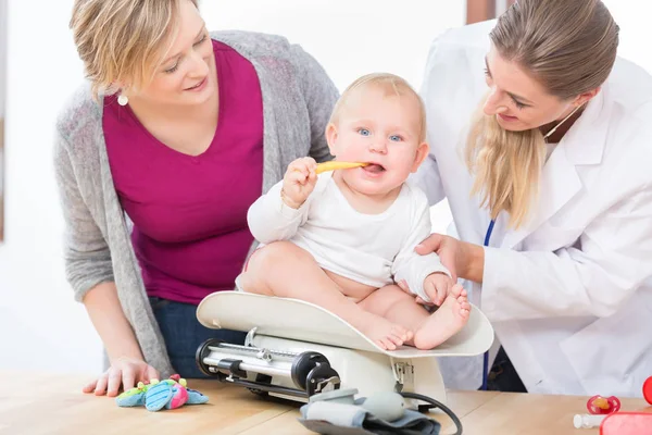 Barnsjukvård specialist ler medan mäta vikten på en flicka — Stockfoto