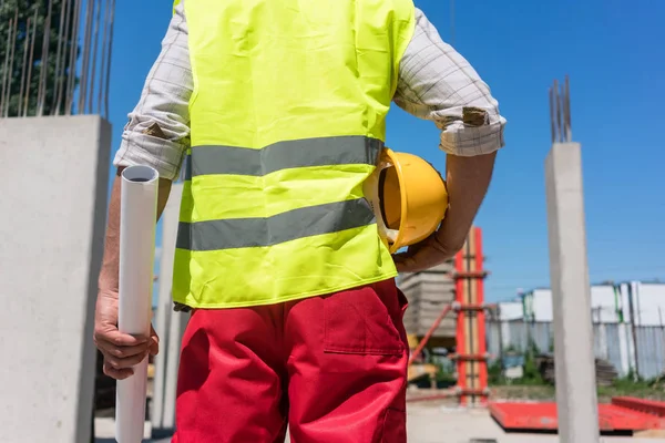 Vista trasera de sección media de un trabajador sosteniendo un plano y un casco amarillo —  Fotos de Stock