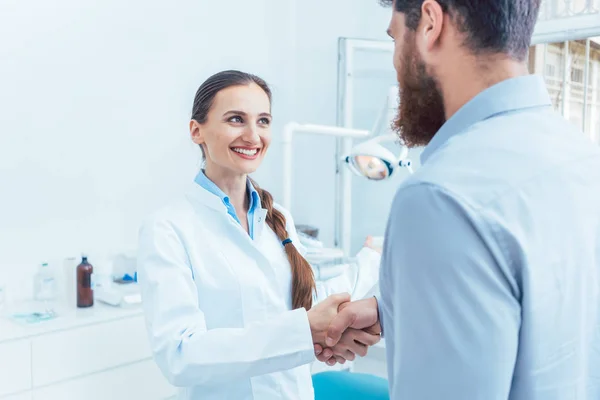 Retrato de um dentista confiável e alegre apertando a mão de um paciente — Fotografia de Stock