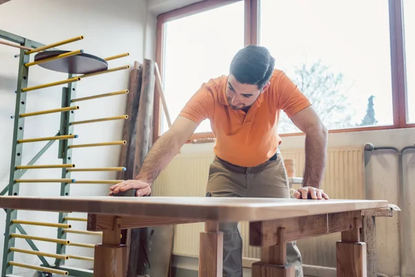 Carpenter polishing and varnishing a table — Stock Photo, Image