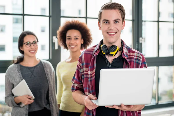 Retrato del joven sonriendo mientras sostiene un portátil en el trabajo —  Fotos de Stock