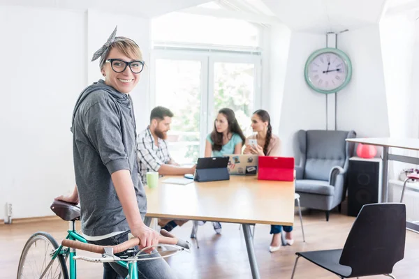 Munter ung kvinne som holder sin pendlersykkel på et felles kontor – stockfoto