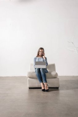 İnwhite Oda smartphone ve dizüstü kullanarak oturan genç kadın