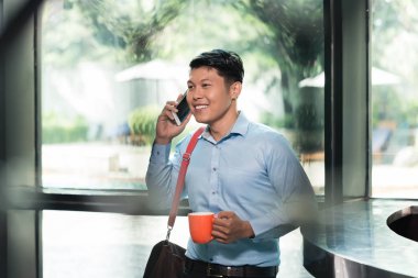 Bir fincan kahve tutarken cep telefonu üzerinde konuşurken neşeli Asya genç adam