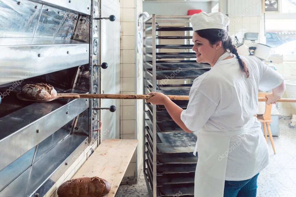Baker woman getting bread out of bakery oven