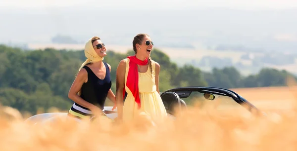 Two women sitting on hood of convertible car — Stock Photo, Image